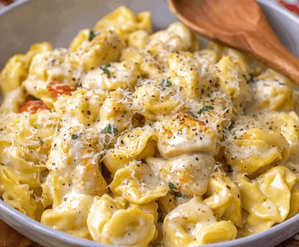 Creamy garlic Parmesan chicken tortellini dish garnished with fresh herbs, featuring tender pasta, grilled chicken, and melted cheese in a flavorful sauce.