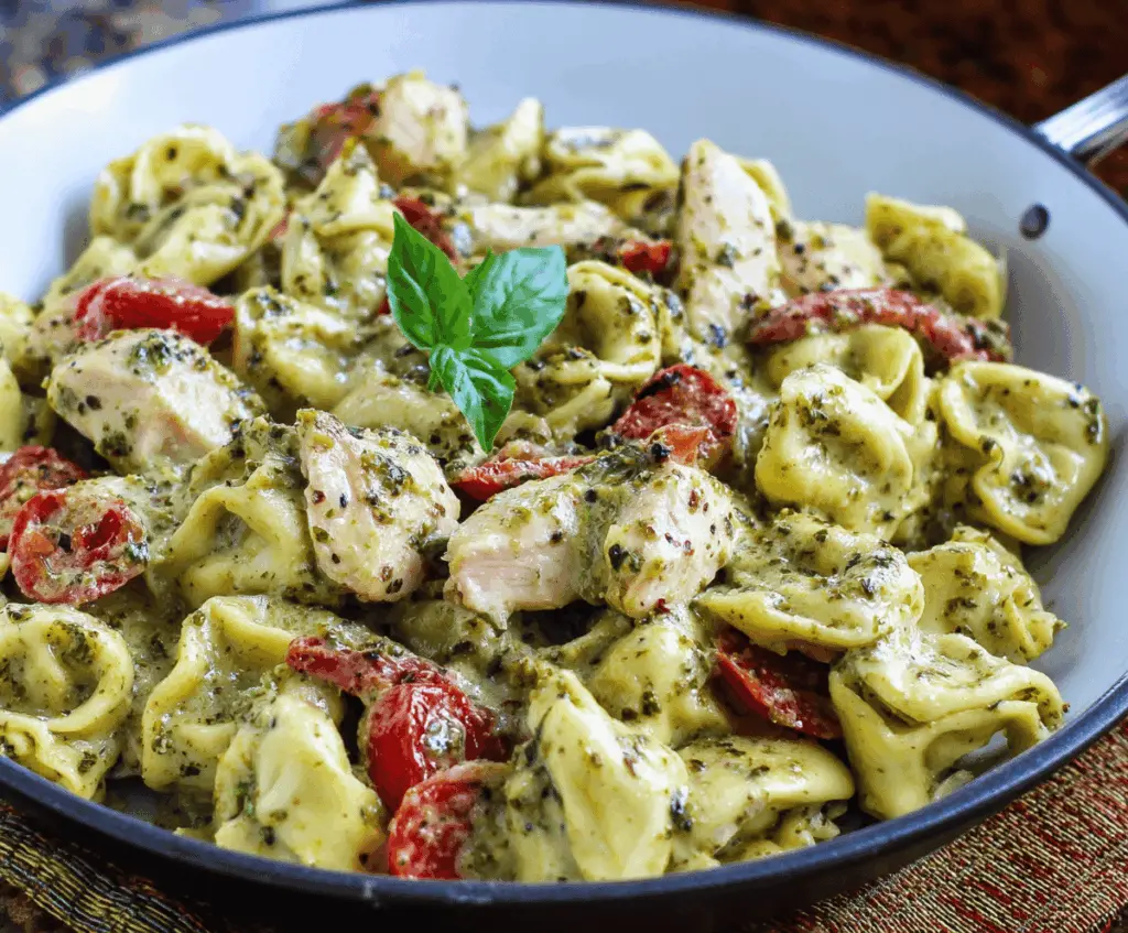 Creamy pesto chicken tortellini served on a plate garnished with fresh basil and Parmesan cheese, featuring tender pasta filled with cheese and chicken in a vibrant green pesto sauce.