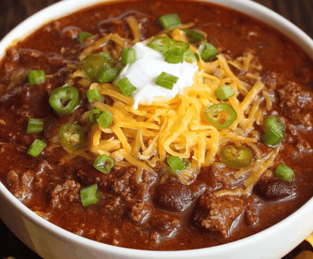 Delicious homemade Texas Roadhouse chili with or without beans served in a bowl, topped with shredded cheese and fresh herbs