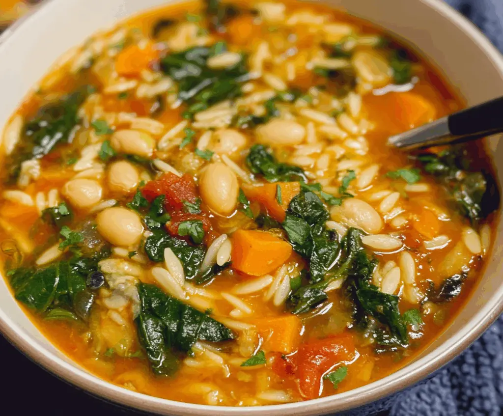 A bowl of vegetable orzo soup with colorful vegetables and tender pasta in a clear broth.