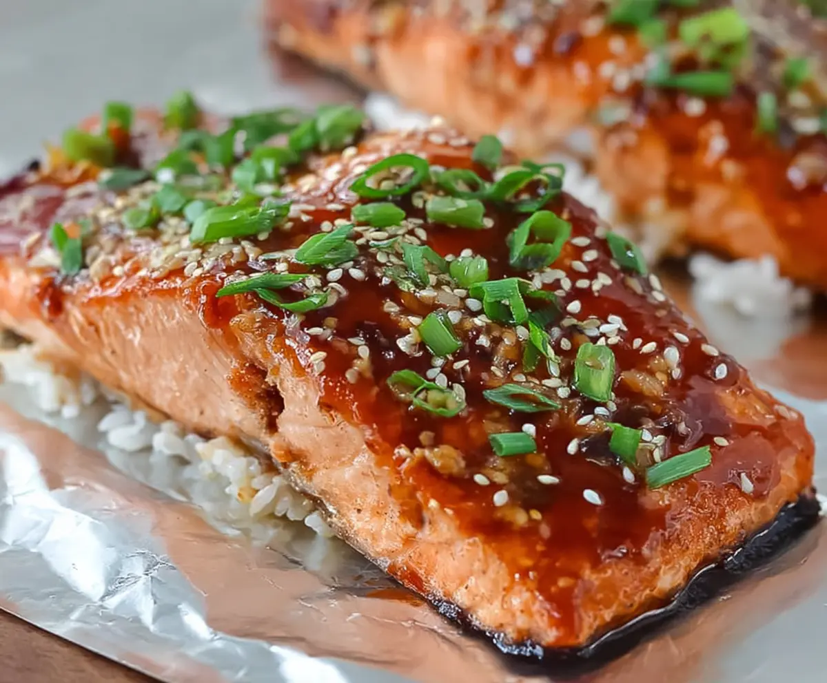 Delicious glazed teriyaki salmon fillet garnished with sesame seeds and green onions on a white plate.